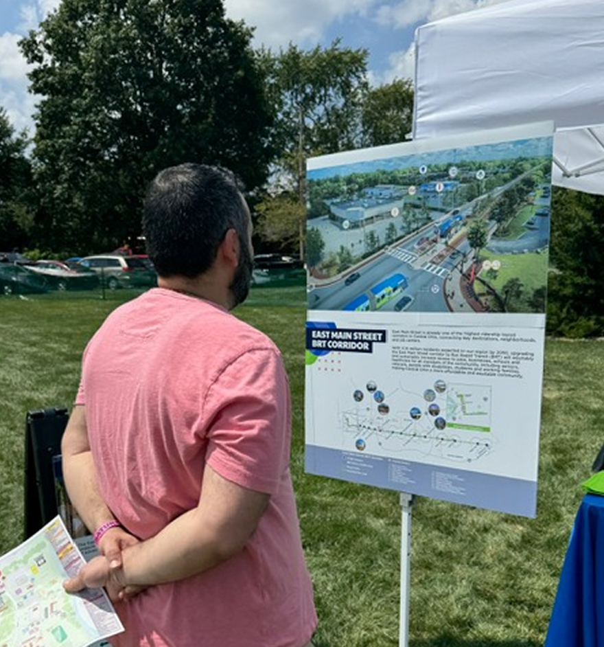 Community member reviewing a project display board at an outdoor engagement event near a waterfront.
